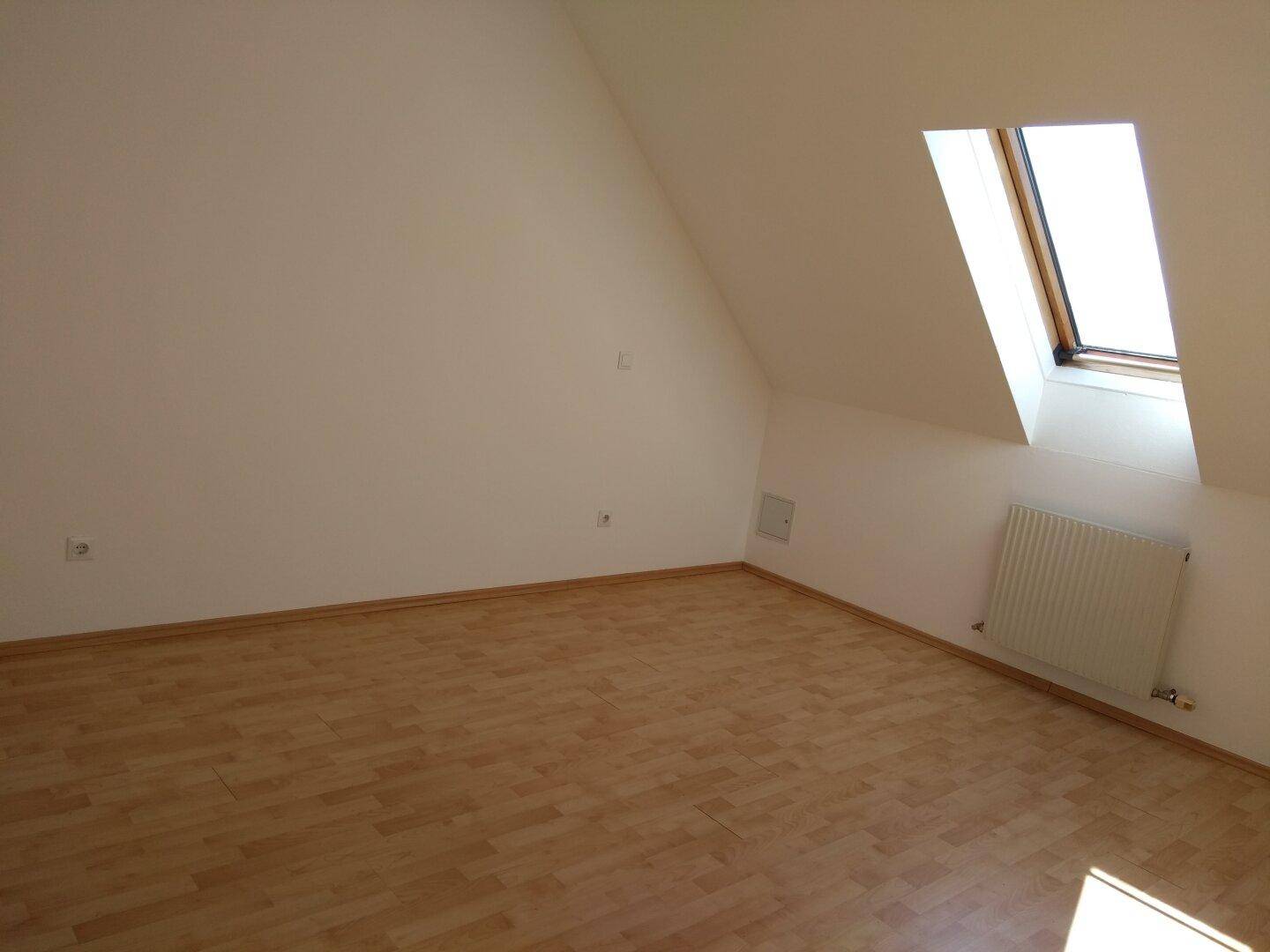 Helles Schlafzimmer im Dachgeschoss mit Laminatboden, Dachfenster und Heizkörper.