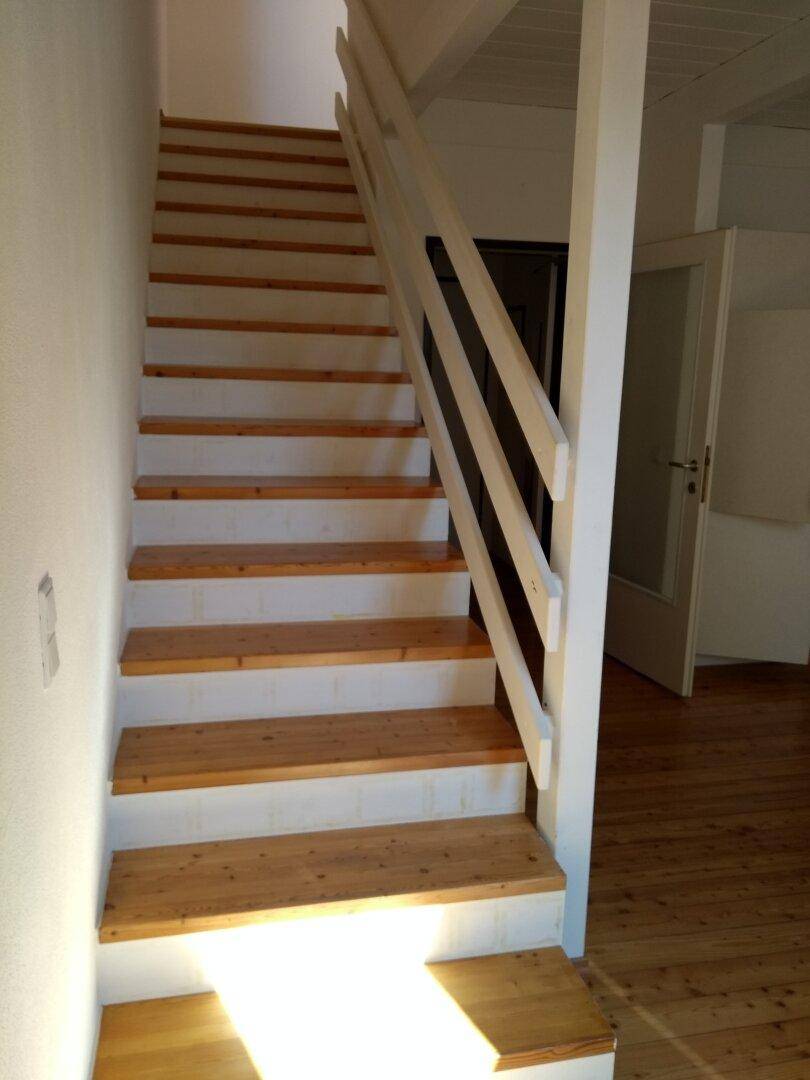 Helle Holztreppe mit weißem Geländer, die verschiedene Ebenen des Hauses verbindet.