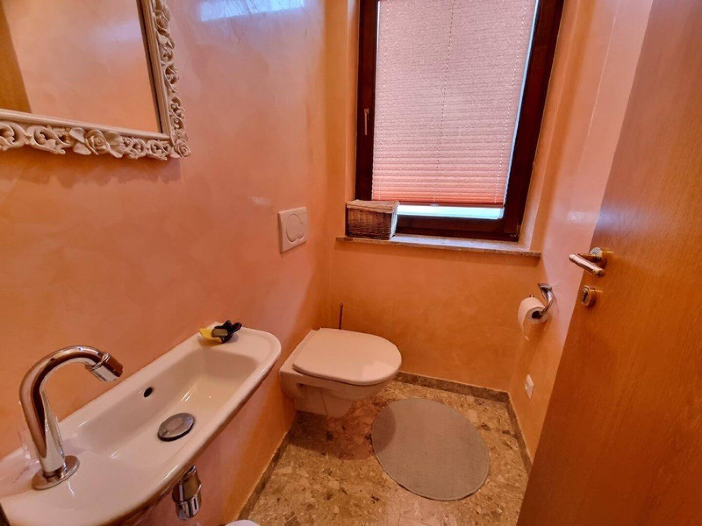 Kleines Gäste-WC mit Waschbecken, Toilette und Fenster in warmen Farbtönen.