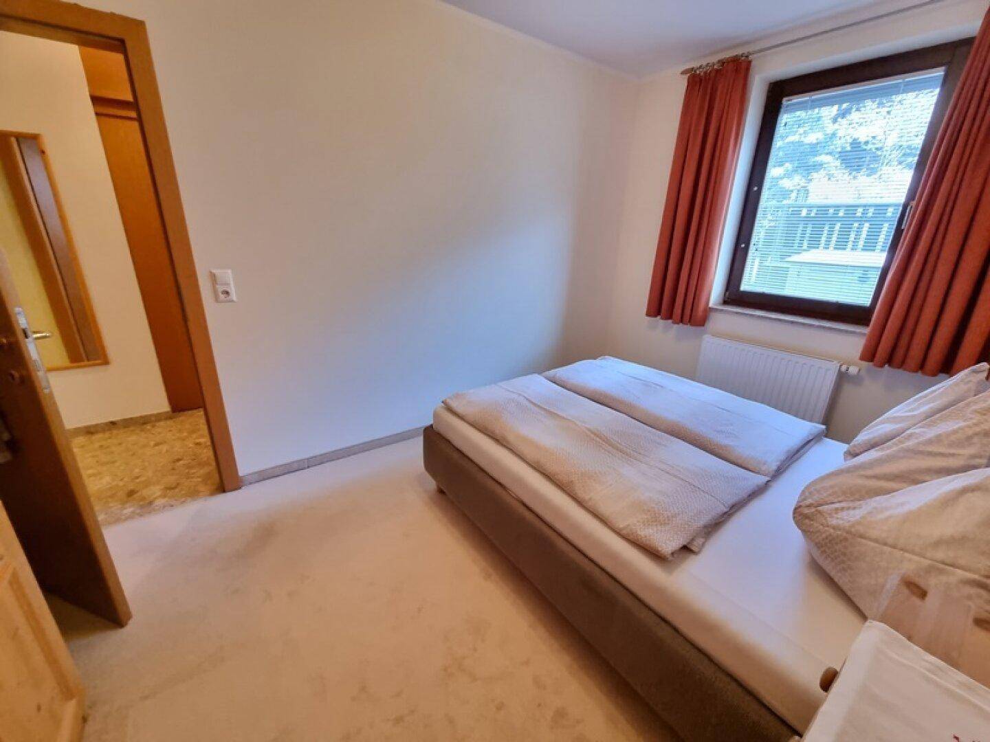 Gemütliches Schlafzimmer mit Einzelbett, Teppichboden und Fenster mit Vorhängen.