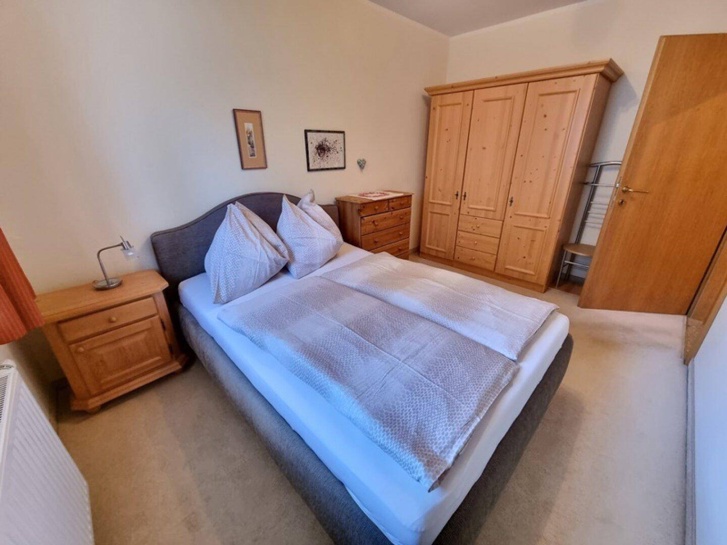 Schlafzimmer mit Doppelbett, Holzschrank und Nachttischen, in hellem Ambiente.