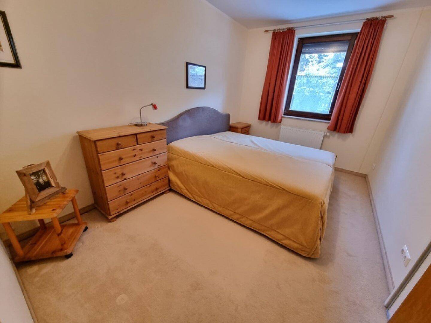 Schlafzimmer mit Einzelbett, Kommode und Fenster, in schlichter und funktionaler Einrichtung.