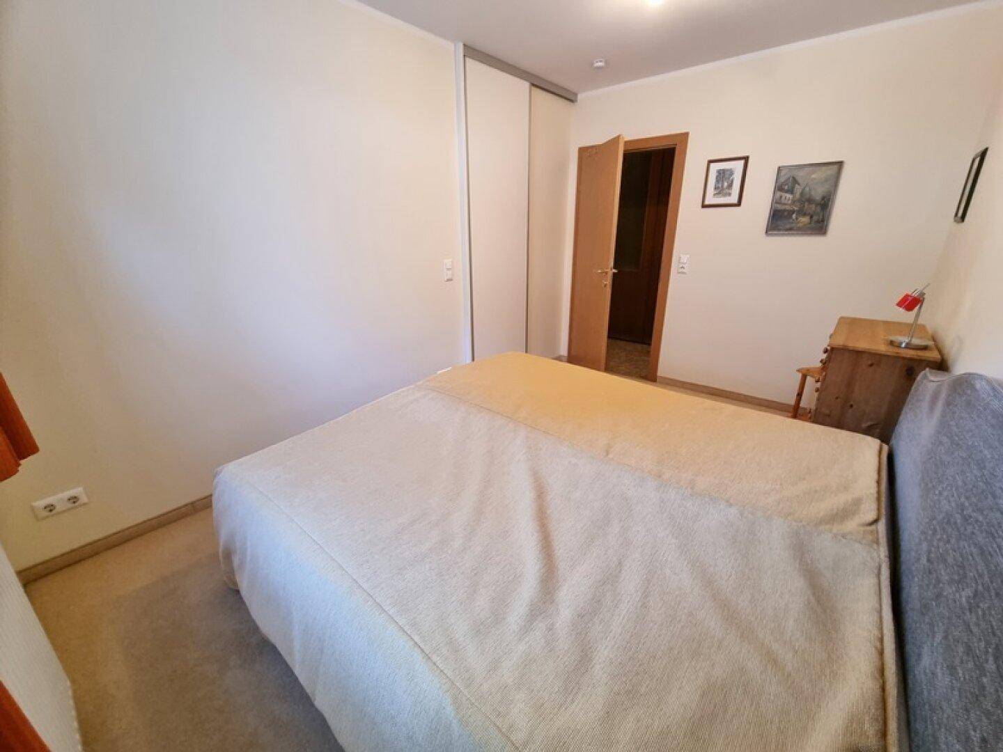 Schlafzimmer mit Doppelbett und Schiebetürenschrank, in neutralen Farben gehalten.