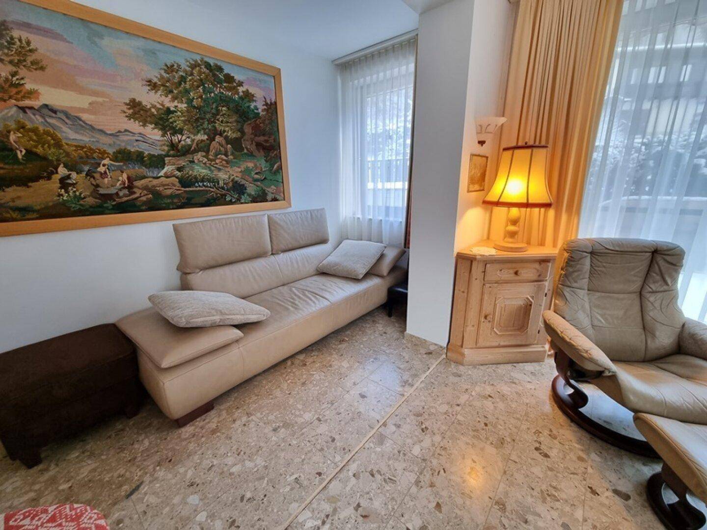 Wohnzimmer mit beigem Sofa, Sessel und großem Wandteppich, hell und einladend.