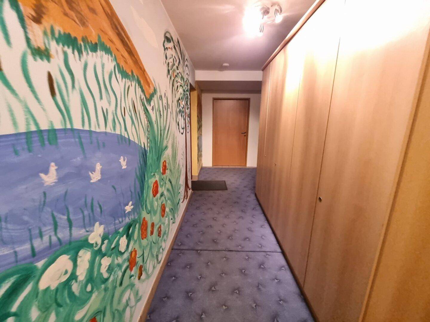 Flur mit farbenfroher Wandmalerei und Holzschränken, einladend und individuell gestaltet.