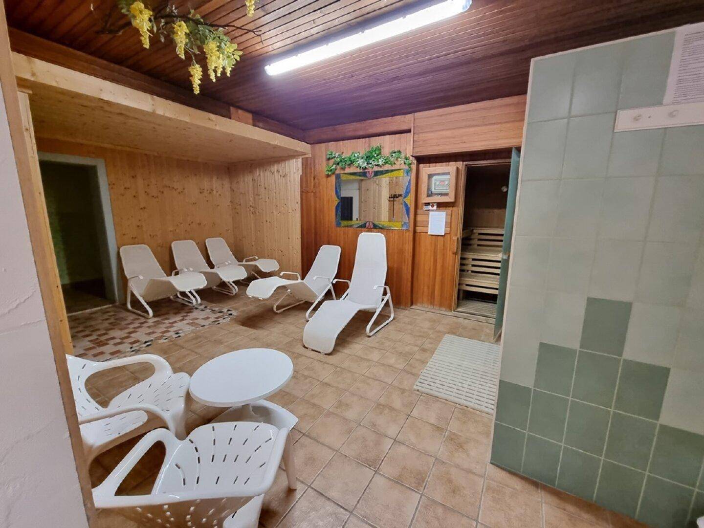 Entspannungsbereich mit Holzvertäfelung, Liegestühlen und Zugang zur Sauna.