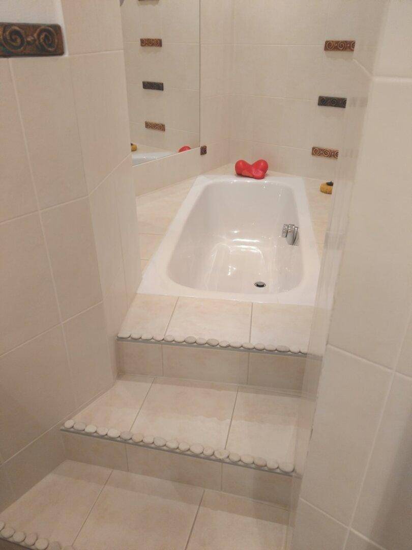 Badezimmer mit eingebauter Badewanne und gefliesten Stufen, hell und funktional.