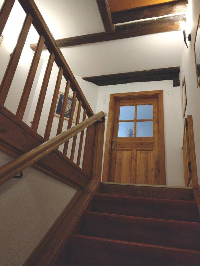 Holztreppe mit Teppich und Holztür, die zu einem weiteren Bereich führt.