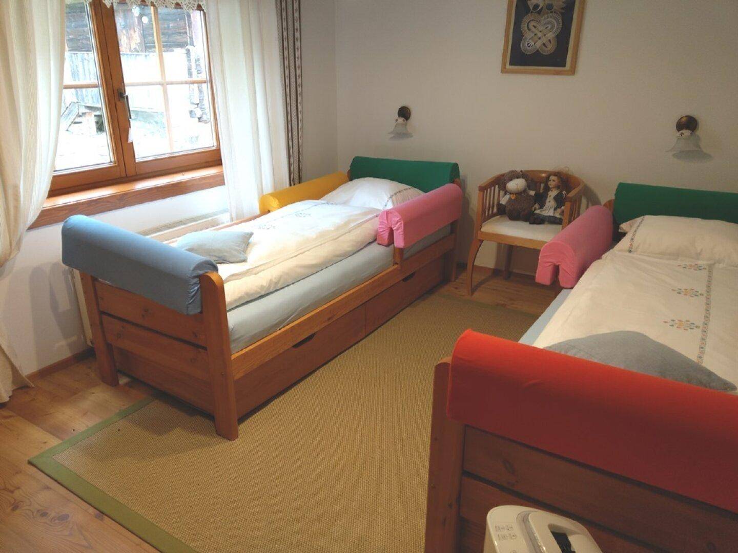 Kinderzimmer mit zwei Einzelbetten, Holzmöbeln und Blick nach draußen.