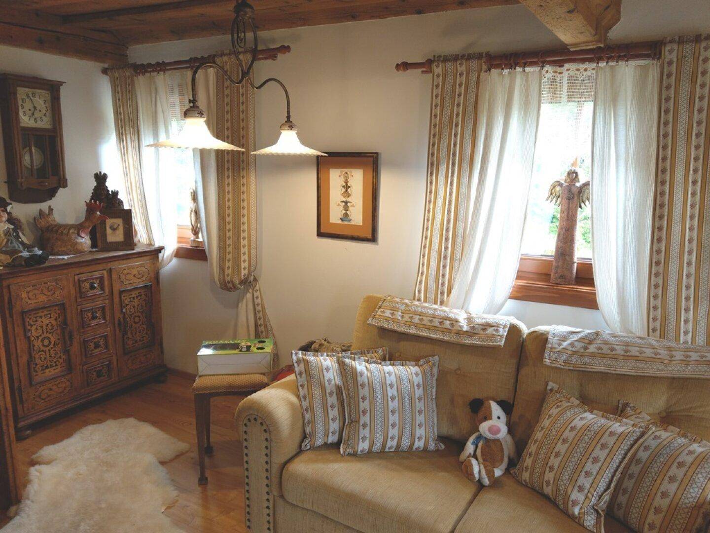 Gemütliches Wohnzimmer mit Holzbalkendecke, Sofa und traditionellen Holzmöbeln.