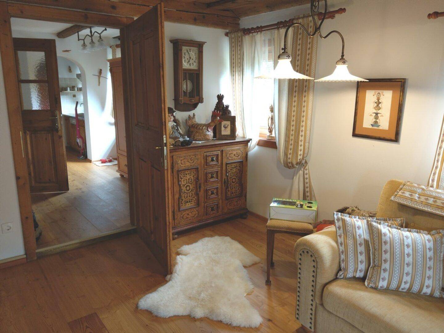 Wohnzimmer mit Holzbalkendecke, traditionellen Möbeln und Zugang zu einem weiteren Raum.