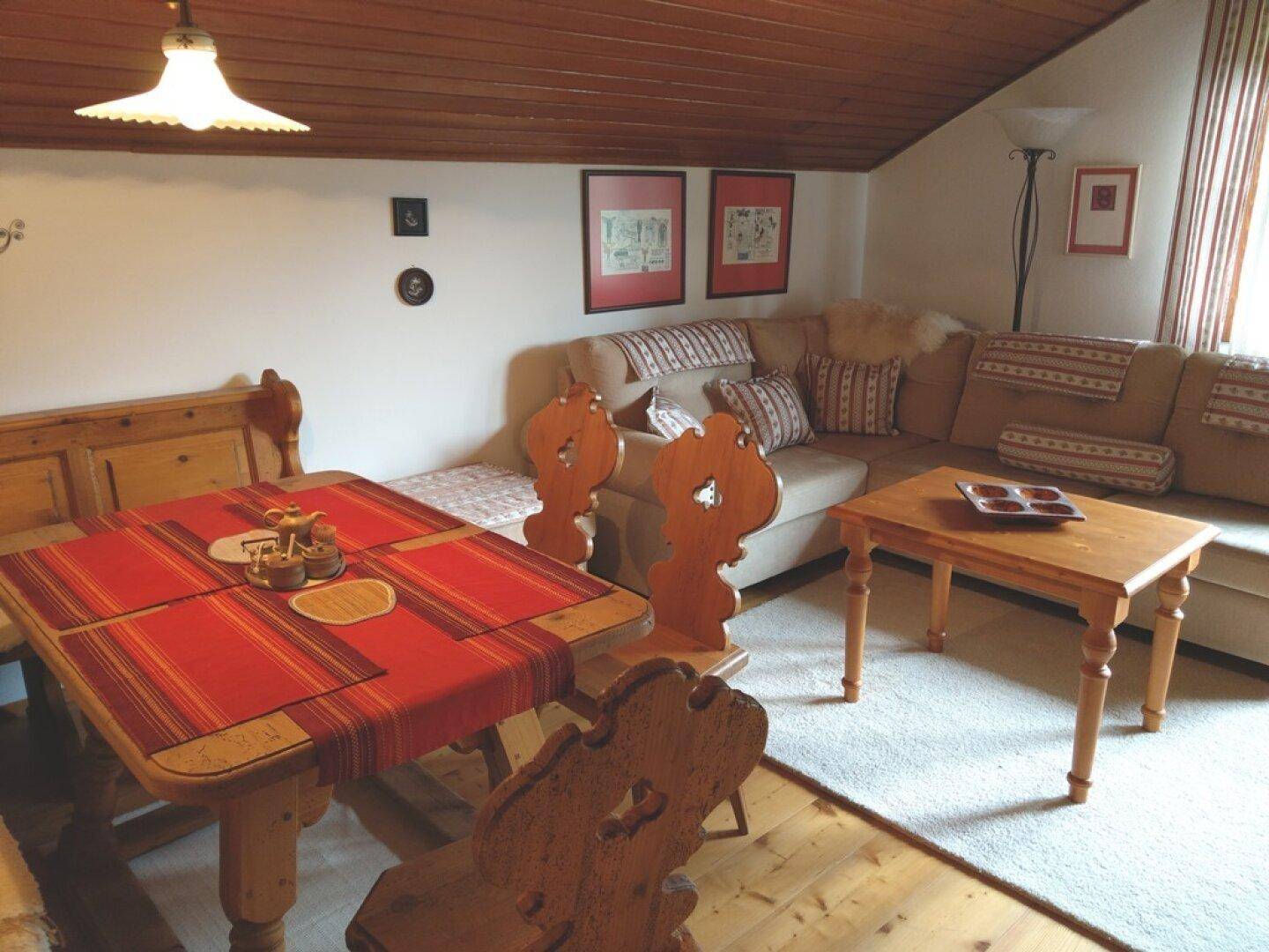 Gemütlicher Wohn- und Essbereich im Dachgeschoss mit Holzbalkendecke und traditionellen Möbeln.