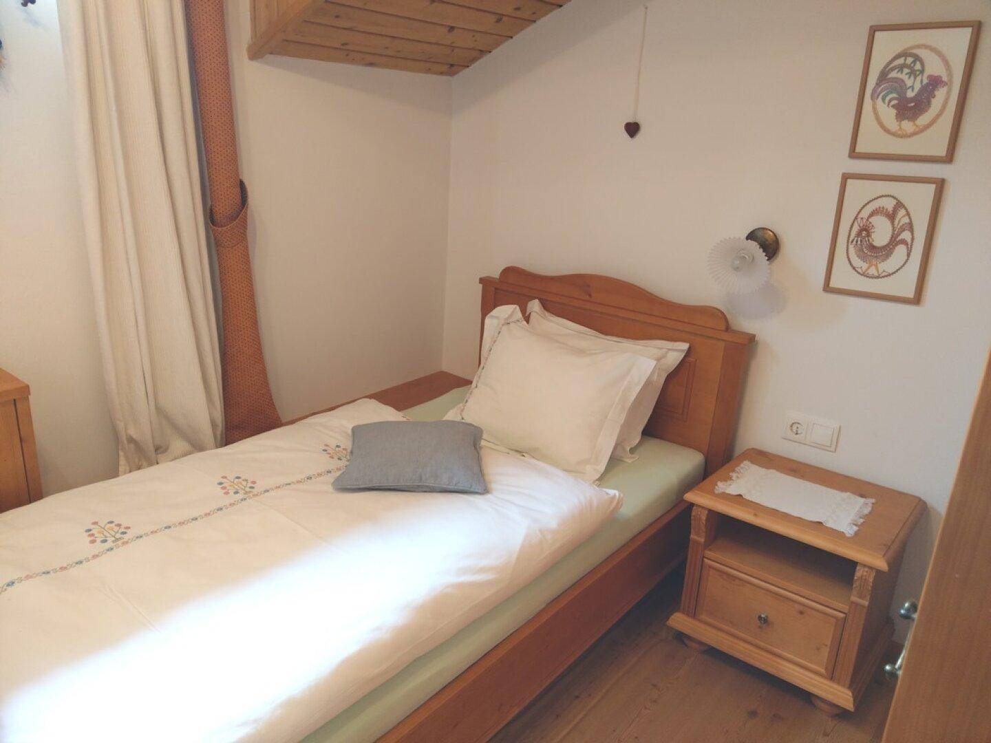Einzelzimmer im Dachgeschoss mit Holzbett, Nachttisch und schräger Decke.