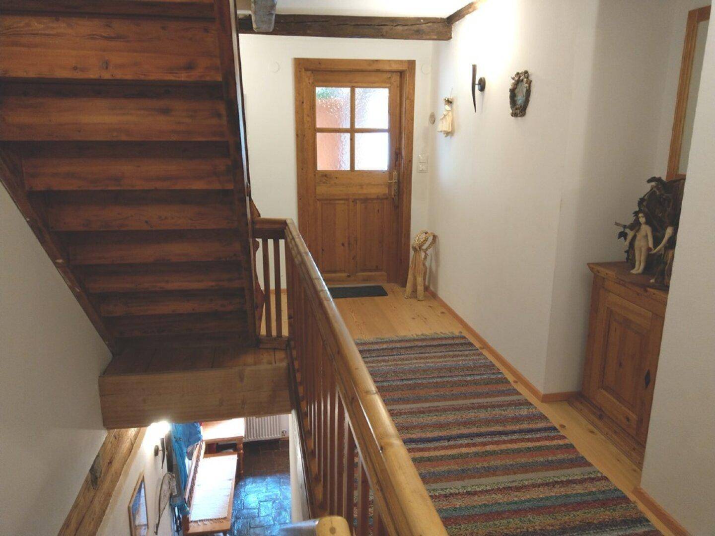Holztreppe mit Teppichläufer, die in die obere Etage führt.