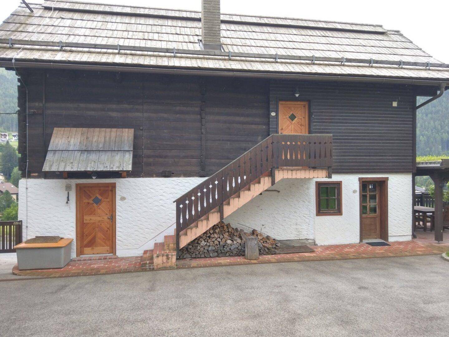 Traditionelles Holzhaus mit Außentreppe und überdachtem Sitzbereich im Freien.