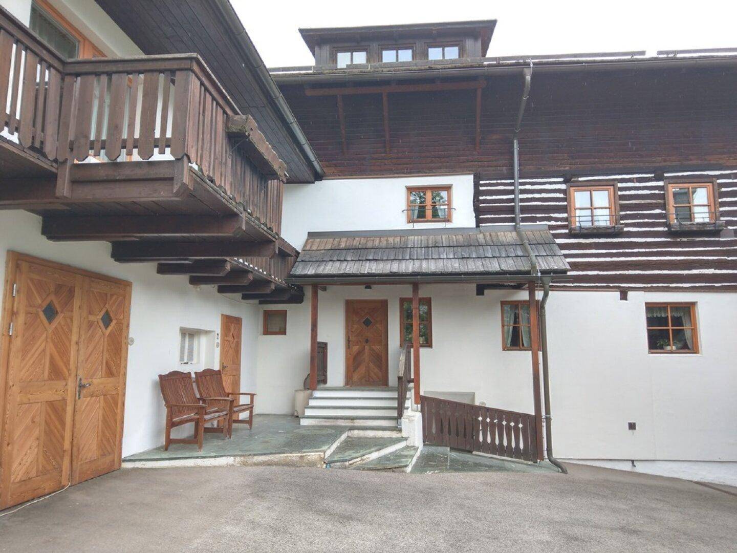 Traditionelles Holzhaus mit Balkonen und Außentreppe, umgeben von Natur.
