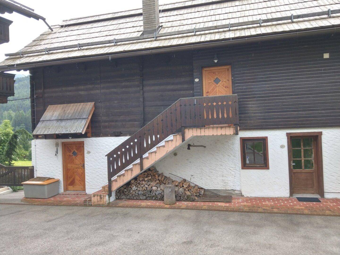 Traditionelles Holzhaus mit Außentreppe, Holzstapel und überdachtem Sitzbereich.