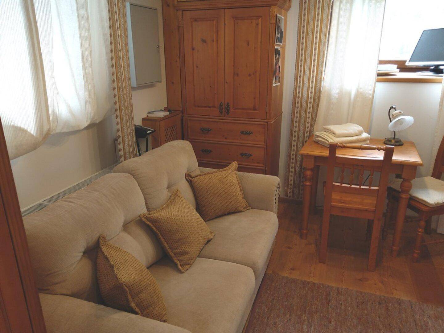 Gemütliches Wohnzimmer mit Sofa, Schrank und kleinem Schreibtisch.