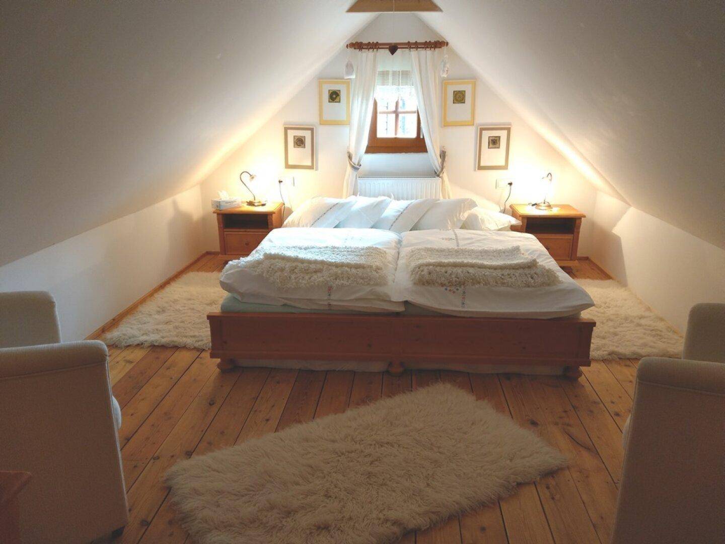 Schlafzimmer im Dachgeschoss mit Doppelbett, schrägen Wänden und Holzboden.