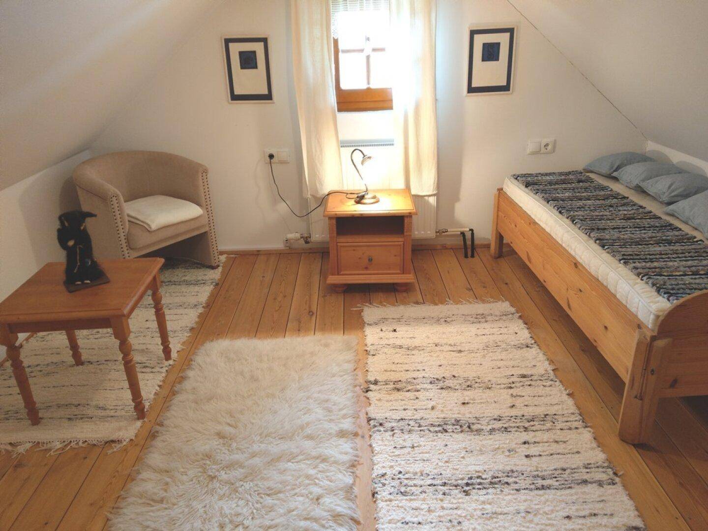 Schlafzimmer im Dachgeschoss mit Einzelbett, Sessel und Holzboden.