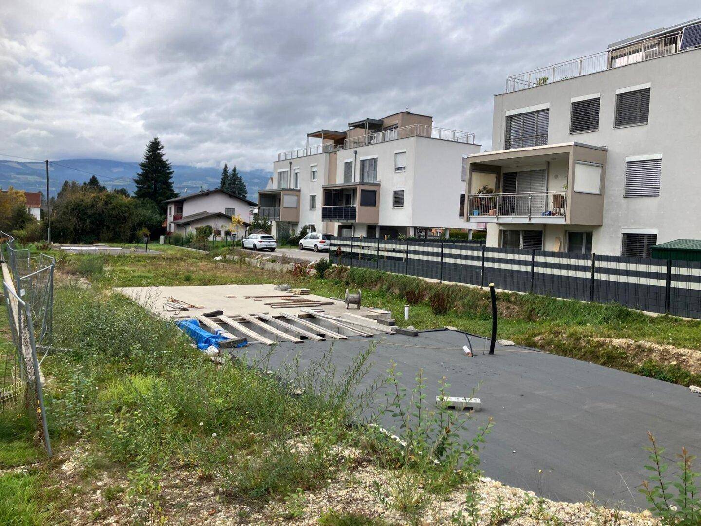 Weitläufiges Baugrundstück in einer Wohngegend, umgeben von modernen Mehrfamilienhäusern mit Balkonen und Fernblick.