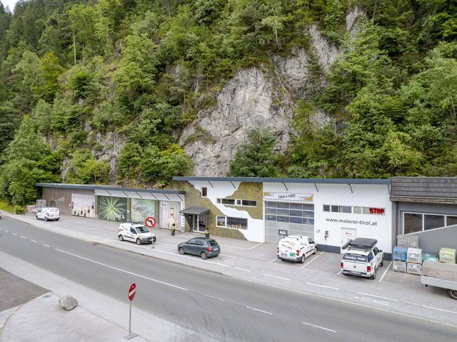 Übersicht des Gewerbeobjekts mit Parkplätzen und der umliegenden Berglandschaft.