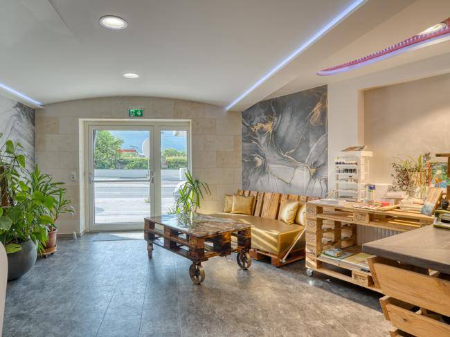 Lounge- oder Wartebereich mit Palettenmöbeln, großen Glastüren und dekorativer Wandverkleidung.
