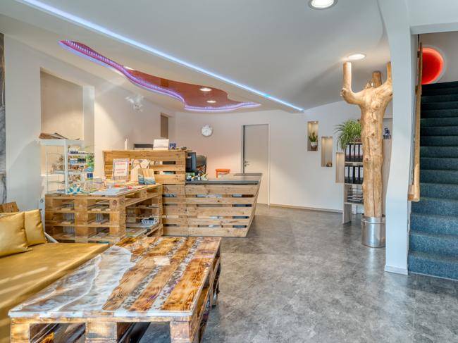 Empfangsbereich mit Theke und Couchtisch aus Holzpaletten, Baumstamm-Dekoration und LED-Beleuchtung.