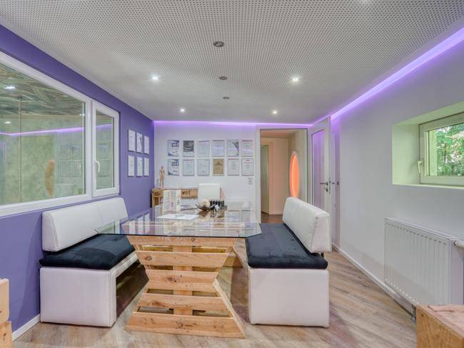 Besprechungsraum mit Glastisch, Sitzbänken, lila Akzentwand und LED-Beleuchtung.