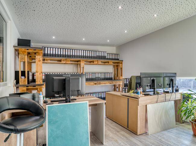 Büro mit mehreren Computermonitoren, Regalen aus Holzpaletten und hellem Boden.