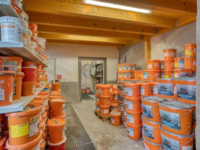 Lagerraum mit sichtbaren Holzdeckenbalken und Regalen voller Farbeimer.