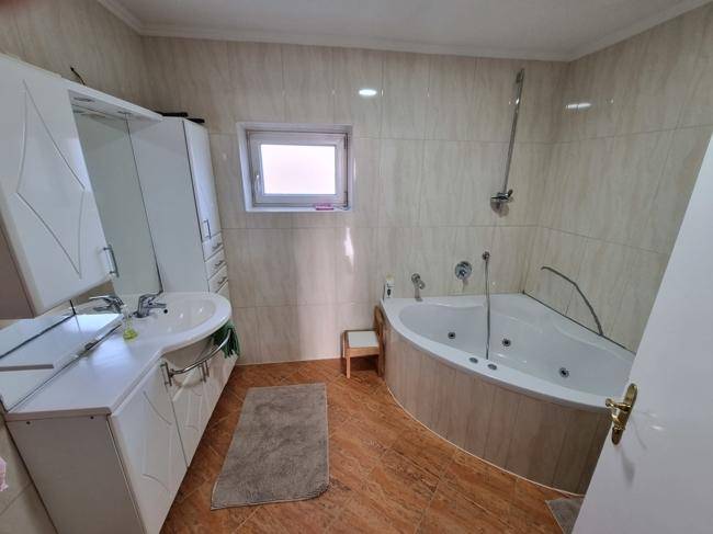 Badezimmer mit Eckbadewanne, Duschfunktion, Einzelwaschbecken und einem kleinen Fenster.