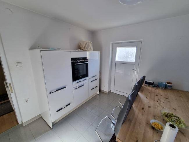 Moderne weiße Einbauküche mit Hochglanzfronten, integriertem Backofen und grauen Fliesenboden.