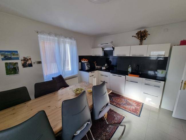 Helle Küche mit weißer Einbauküche, Esstisch und Fenster, ideal für gemeinsame Mahlzeiten.