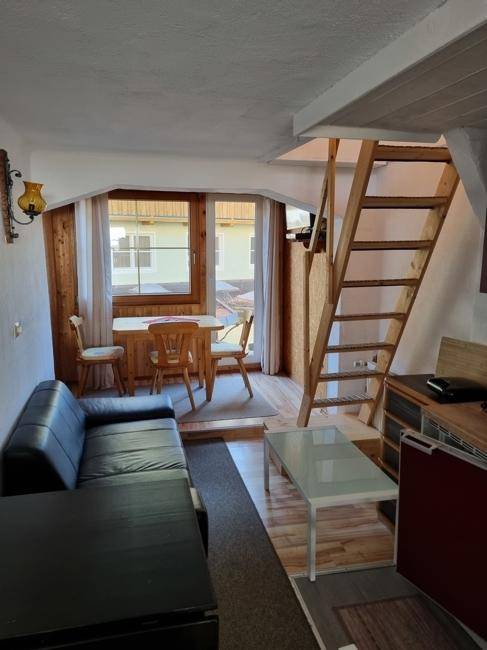 Kleiner, gemütlicher Wohnbereich mit Sofa, Esstisch und einer Holztreppe zur oberen Etage.