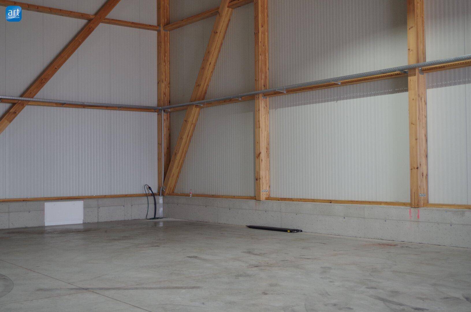 Geräumiger Innenbereich mit hohen Decken, Betonboden und Holztragwerk, ideal für Lagerung oder Werkstatt.