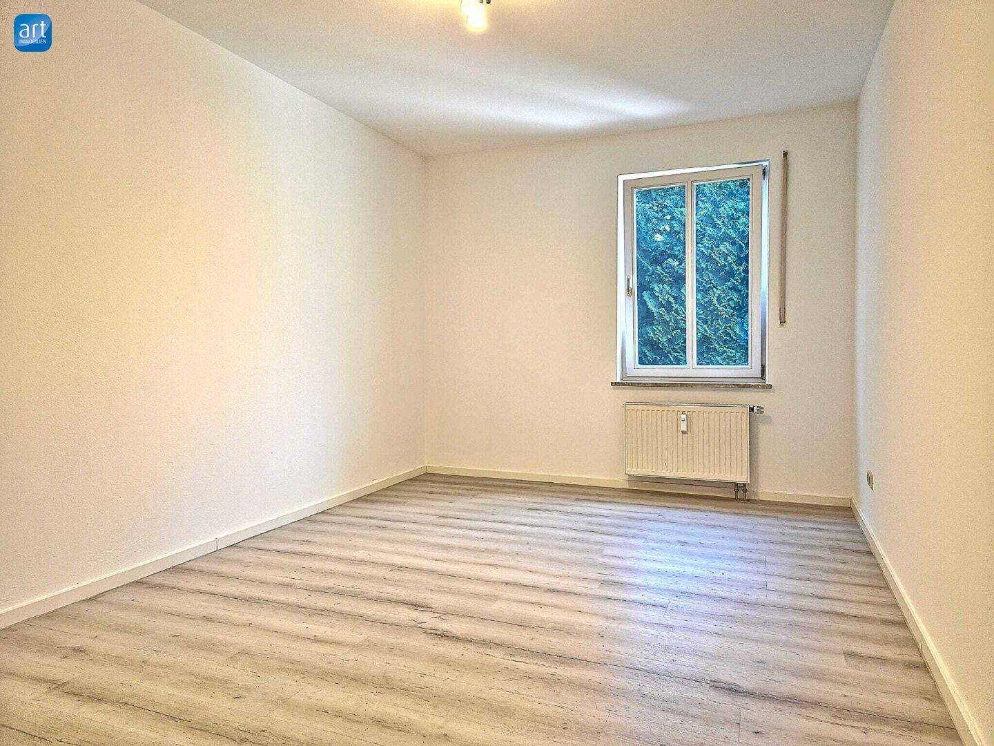 Geräumiges Schlafzimmer mit Laminatboden und einem Fenster mit Blick ins Grüne.