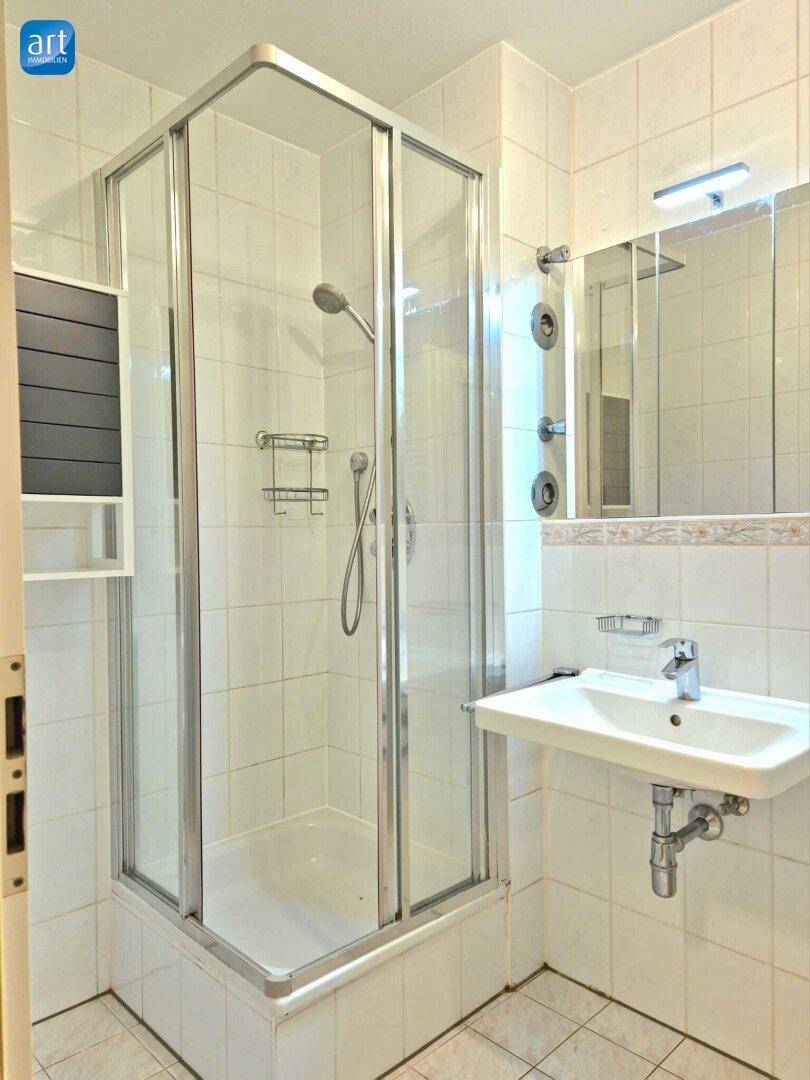 Badezimmer mit Duschkabine, Waschbecken und Spiegelschrank in hellen Fliesen.