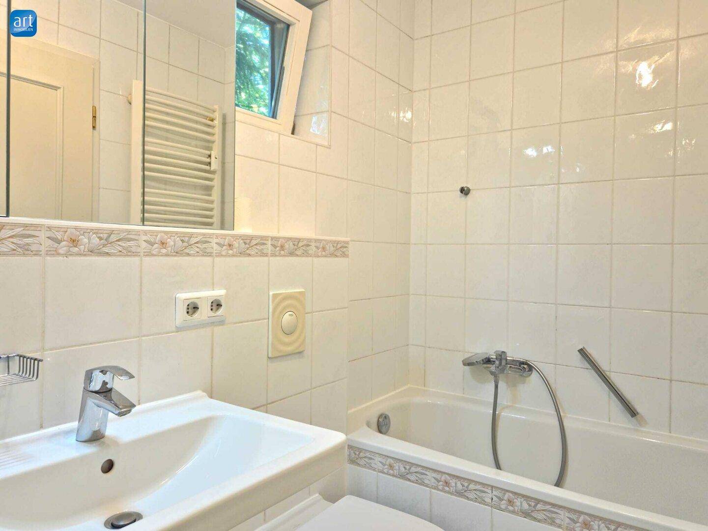 Badezimmer mit Badewanne, Waschbecken, beheiztem Handtuchhalter und Fenster.