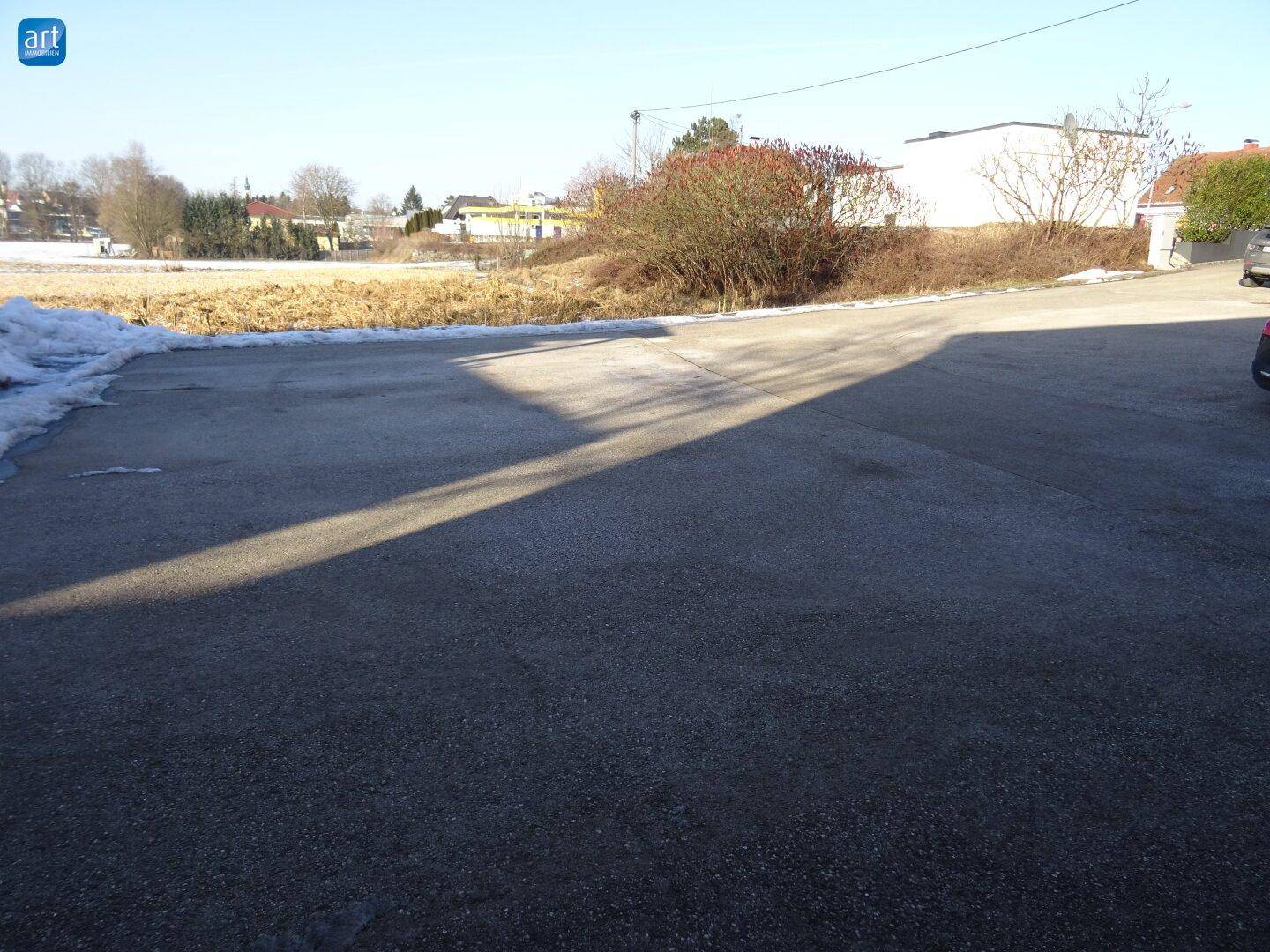 Leerer Parkplatz oder Zufahrt mit Schnee am Rand und weitem Blick auf die ländliche Umgebung.