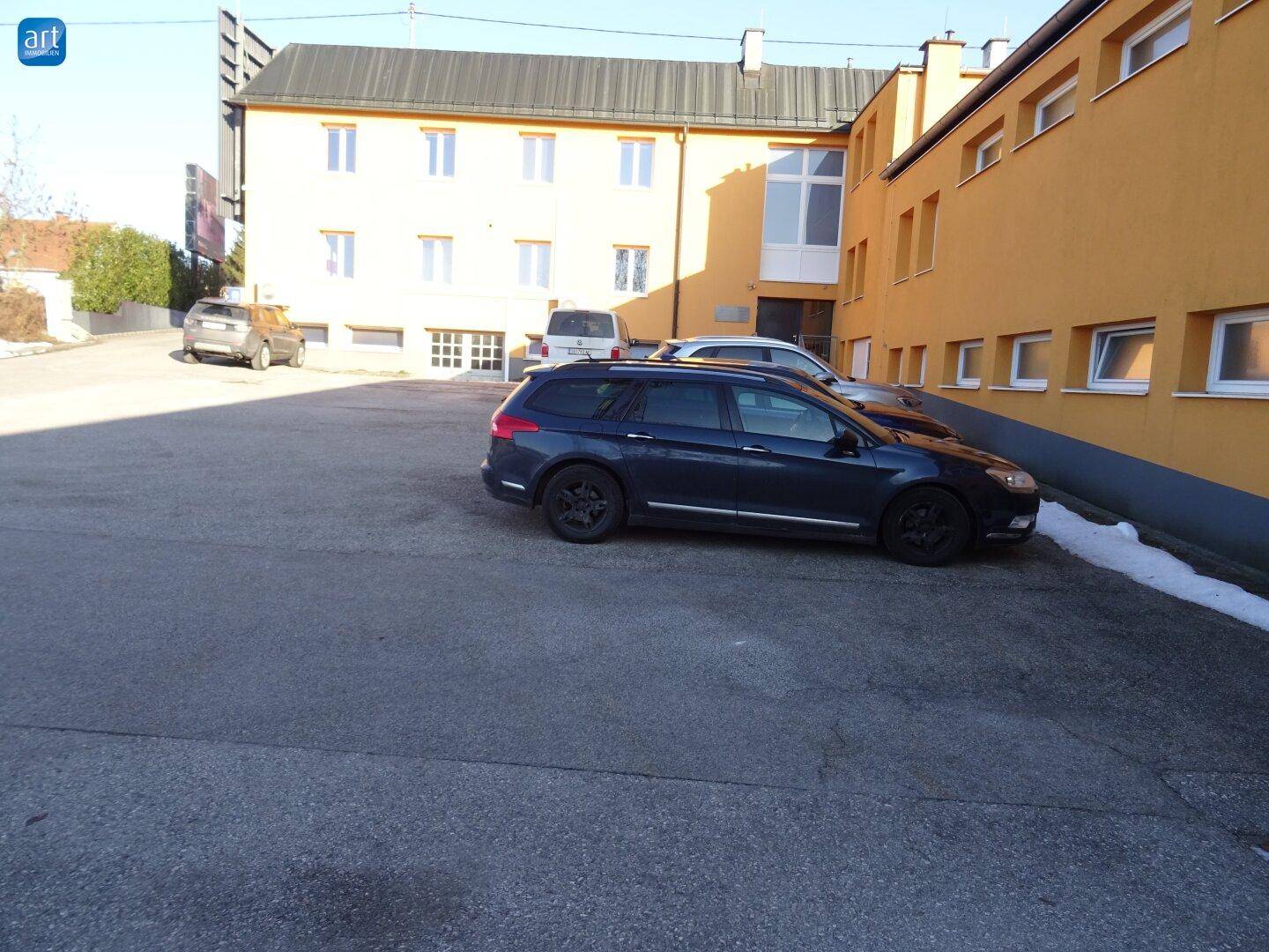 Außenansicht eines Gebäudekomplexes mit großem Parkplatz und abgestellten Fahrzeugen im Winter.