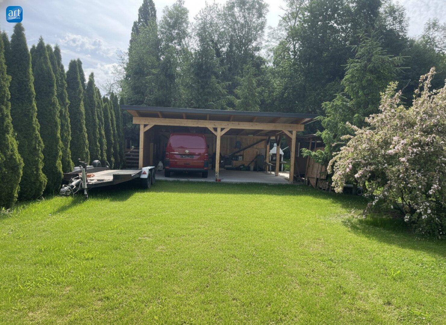 Geräumiger Holzcarport im Garten mit viel Grün und hohen Hecken im Hintergrund, auf Rasenfläche.