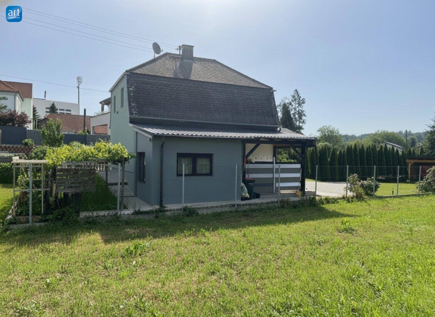 Ansicht des Hauses von der Gartenseite mit überdachtem Bereich und viel Grün im Vordergrund.