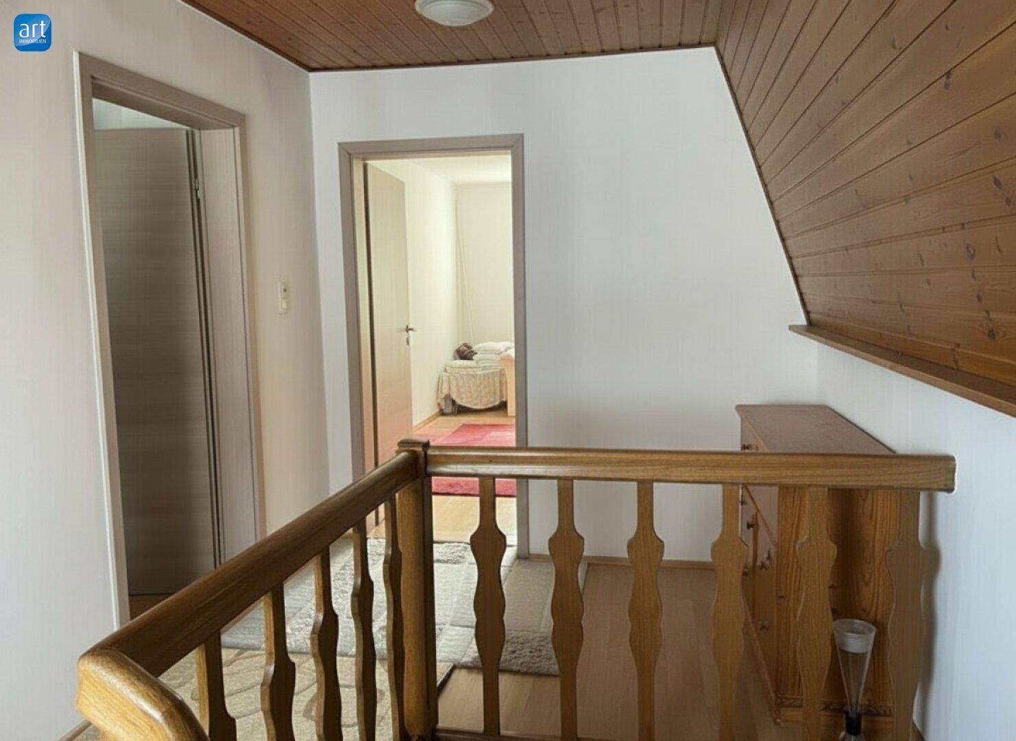 Heller Flur im Obergeschoss mit Holzgeländer, Holzdecke und Zugang zu weiteren Zimmern.