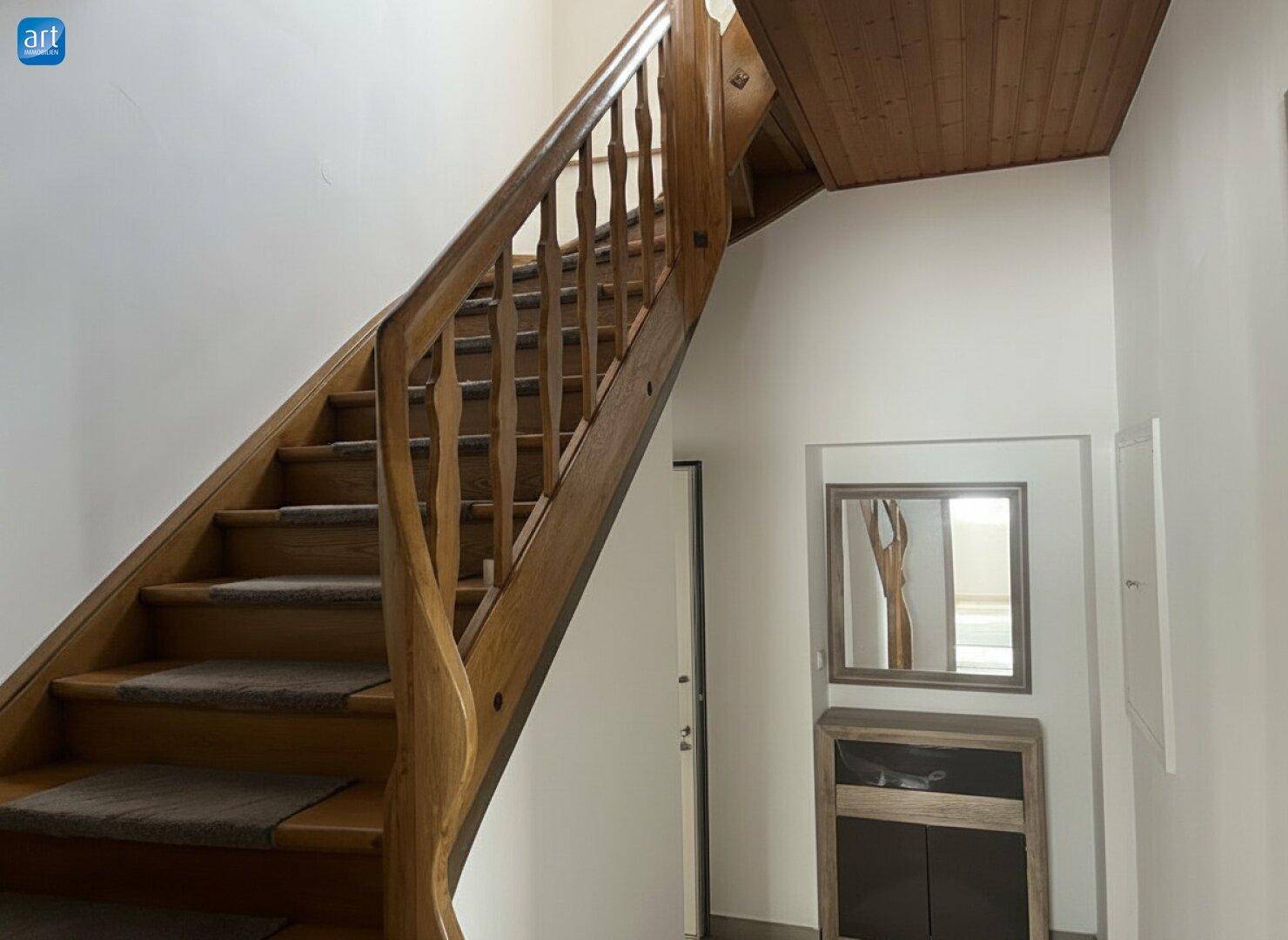 Holztreppe mit Teppichstufen und Holzdecke, die das Erdgeschoss mit dem Obergeschoss verbindet.