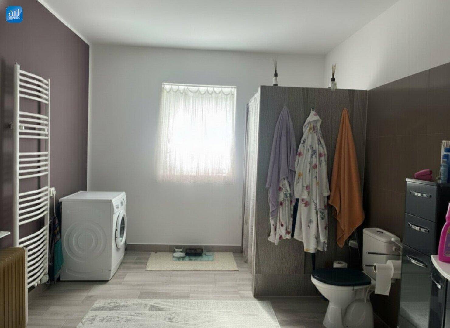 Geräumiges Badezimmer mit Waschmaschine, Toilette und beheiztem Handtuchhalter, hell beleuchtet.