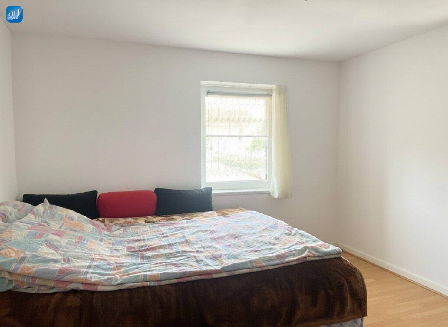 Gemütliches Schlafzimmer mit Doppelbett, Holzboden und einem Fenster mit Blick nach draußen.