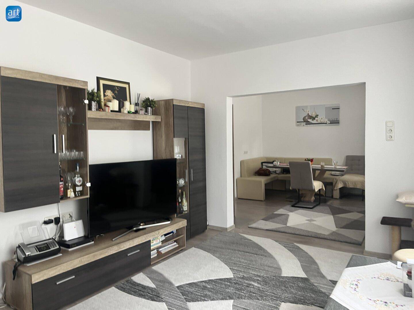 Offener Wohnbereich mit TV-Möbeln und Übergang zu einem Essbereich im Hintergrund.