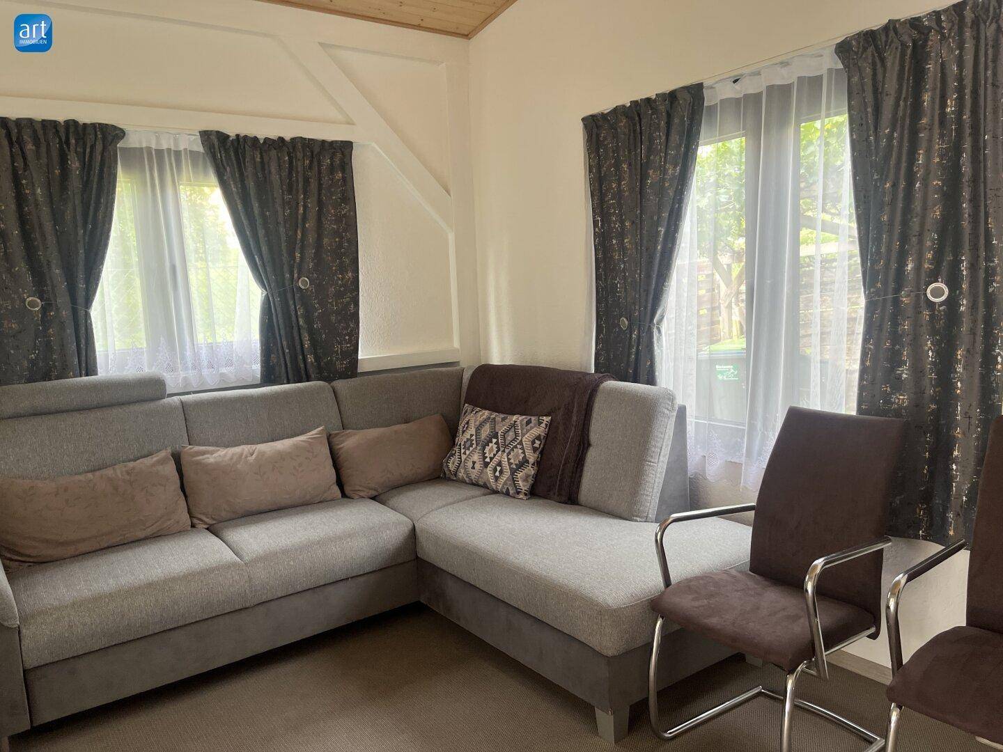 Gemütliches Wohnzimmer mit großem Ecksofa, Holzdecke und Fenstern mit Blick ins Grüne.