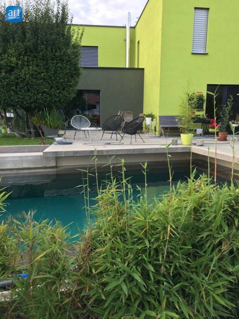 Außenbereich mit modernem Pool, umgeben von üppiger Bepflanzung und einer Terrasse mit Sitzgelegenheiten.